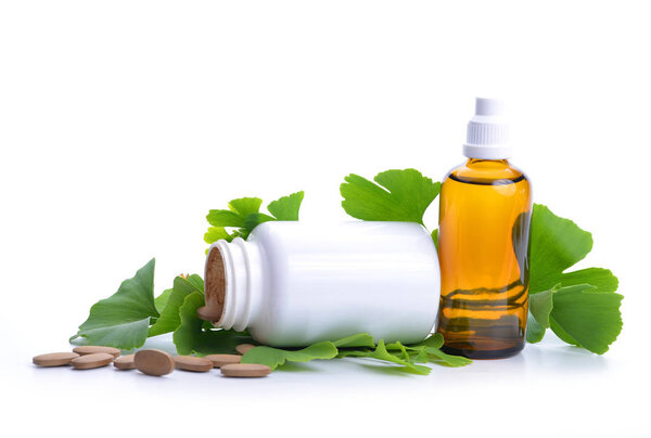 Pills with extract from the ginkgo in bottle and green leaves isolated on a white background.