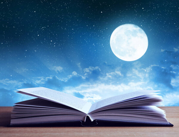 Open book on wooden plank night sky with moon in the background.