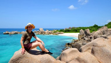 Anse Marron plajı yakınlarındaki granit taşın üzerinde oturan kız, La Digue Adası, Hint Okyanusu, Seyşeller. Tropik tatil.