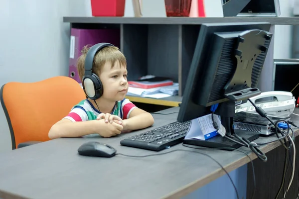 Jongetje met koptelefoon zit op computer in kantoor — Stockfoto