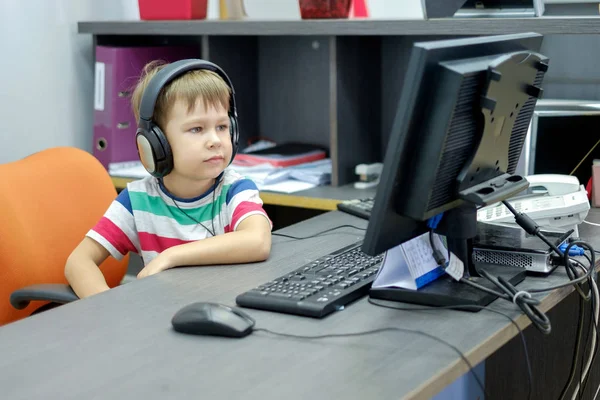 Niño pequeño con auriculares sentado en la computadora en la oficina —  Fotos de Stock