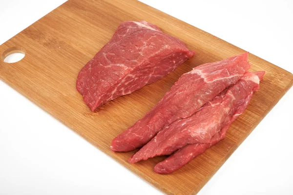 Peça de carne crua e fatias na placa de corte de madeira isolada no fundo branco — Fotografia de Stock
