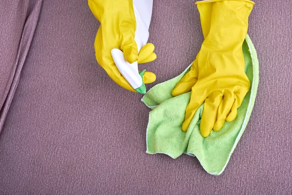 A picture of hands in yellow gloves cleaning the sofa