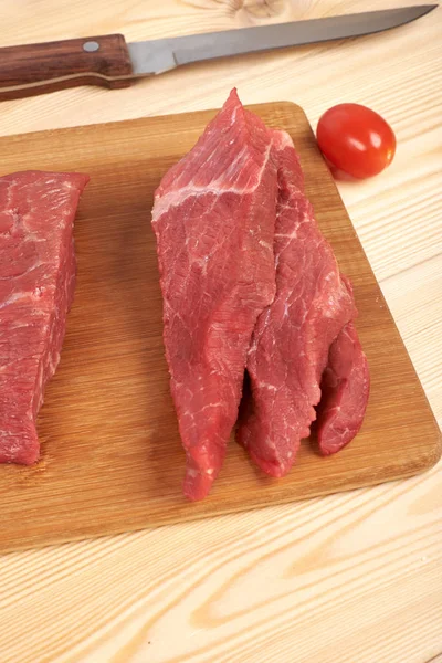 Peça de carne crua e fatias em tábua de corte de madeira — Fotografia de Stock