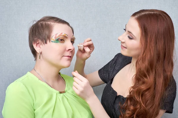 Profesional visage artista aplicación de maquillaje de color en la cara de las mujeres sobre fondo gris . — Foto de Stock