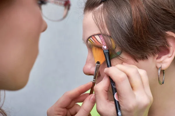 Profesional visage artista aplicación de maquillaje de color en la cara de las mujeres sobre fondo gris . — Foto de Stock