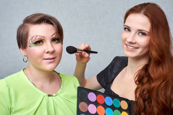 Profesional visage artista aplicación de maquillaje de color en la cara de las mujeres sobre fondo gris . — Foto de Stock