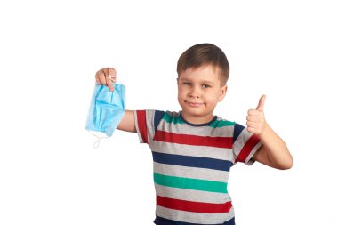 Genç gülümseyen çocuk tıbbi koruyucu maskeyi çıkarıyor ve baş parmağını kaldırıyor. Covid-19 salgını, kendini izole etme konsepti. Karantina kavramı bitti.