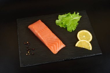 Siyah tahta masada dilimlenmiş somon filetosu, limon ve salata..