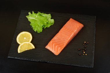 Siyah tahta masada dilimlenmiş somon filetosu, limon ve salata..