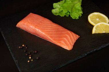 Siyah tahta masada dilimlenmiş somon filetosu, limon ve salata..