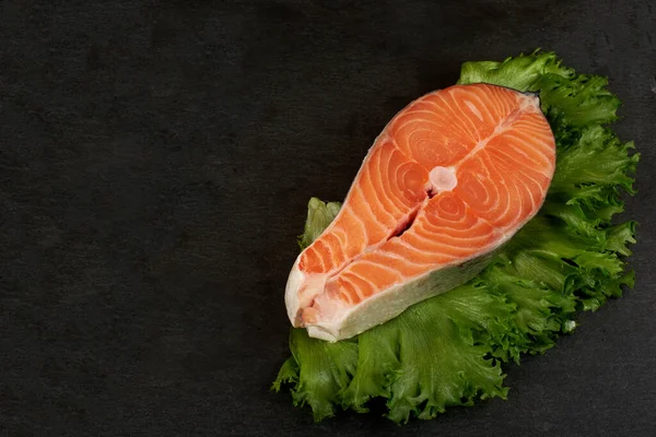 Salmon steak raw fish with a lemon prepared for cooking. Top view on black slate table.