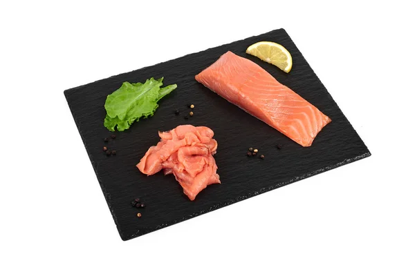 Нарізане філе лосося на чорній сланці, з лимоном і салатом. На білому тлі — стокове фото