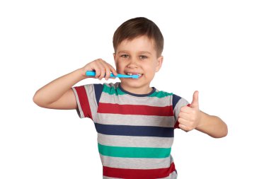 Gülümseyen çocuk dişlerini fırçalıyor ve beyaz arka planda izole bir şekilde baş parmağını gösteriyor.