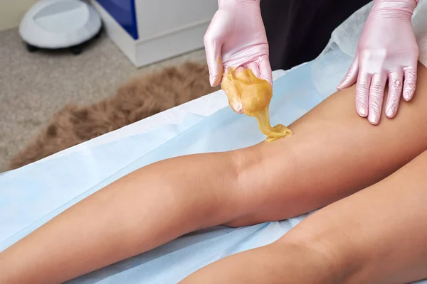 L'esthéticienne se prépare à l'épilation et applique le sucre liquide sur les jambes féminines . — Photo