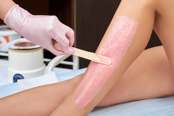 Den kosmetolog förbereder sig för avsättning och applicera krämen med vax pinne på de kvinnliga benen. Kosmetologiska förfaranden i hemmet Royaltyfria Stockbilder