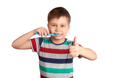 Gülümseyen çocuk dişlerini fırçalıyor ve beyaz arka planda izole bir şekilde baş parmağını gösteriyor.