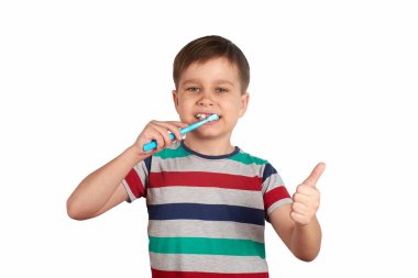 Gülümseyen çocuk dişlerini fırçalıyor ve beyaz arka planda izole bir şekilde baş parmağını gösteriyor.