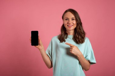 Kız pembe arka planda siyah bir akıllı telefon ekranında parmağını gösteriyor. Boşluğu kopyala