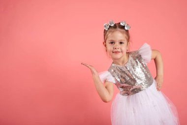 Güzel elbiseli küçük bir kızın portresi. Elleriyle bir yerlerde görünüyor.