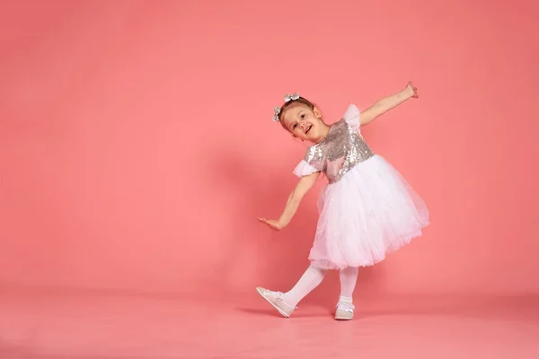 स्टुडिओ मध्ये एक गुलाबी पार्श्वभूमीवर नृत्य एक सुंदर ड्रेस मध्ये लहान मुलगी . — स्टॉक फोटो, इमेज