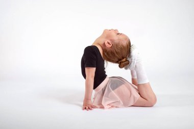 Küçük kız esneme hareketleri yapıyor ve beyaz arka planda jimnastik yapıyor..