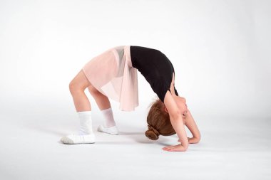 Küçük kız esneme hareketleri yapıyor ve beyaz arka planda jimnastik yapıyor..