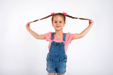 Sevimli küçük bir kız, beyaz arka planda saçlarını savurup çekiyor.