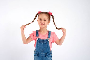 Sevimli küçük bir kız, beyaz arka planda saçlarını savurup çekiyor.