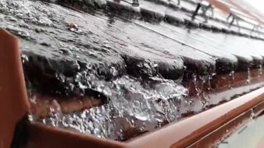 Şiddetli bir yağmur fırtınası, yavaş çekim videosu sırasında çatıdan su birikintisine dökülüyor..