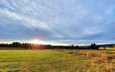 Sumava Ulusal Parkı 'ndaki Kvilda köyü yakınlarındaki çayır ve ormanın üzerinde güzel bir günbatımı..