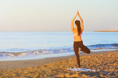 Güneş doğarken pratik Yoga sahilde genç sağlıklı kadın.