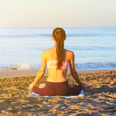 Güneş doğarken pratik Yoga sahilde genç sağlıklı kadın.
