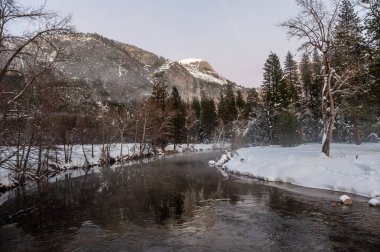 Yosemite Vadisi, gün batımında ürkütücü bir atmosfer sağlayan Merced Nehri 'nin üzerinde asılı ince bir sis tabakasıyla kaplıdır..