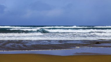Bir sörf, bulutlu havalarda Atlantik Okyanusu kıyısında pitoresk dalgalar