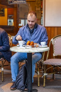 Paris, Fransa, üzerinde 26 Ekim 2018. Sabahları tipik Paris Caddesi. Genç adam yiyor ve açık havada kafede bir dinlenme vardır.