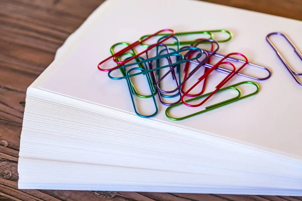 Big multi-colored, office paper clips on a pile of sheets of white paper