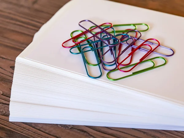 Big multi-colored, office paper clips on a pile of sheets of white paper