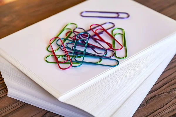 Big multi-colored, office paper clips on a pile of sheets of white paper