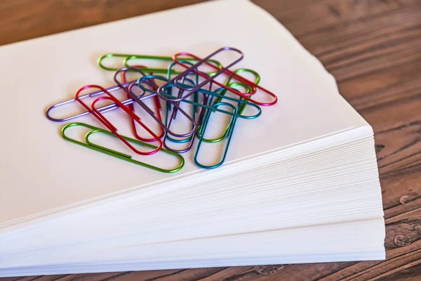 Big multi-colored, office paper clips on a pile of sheets of white paper