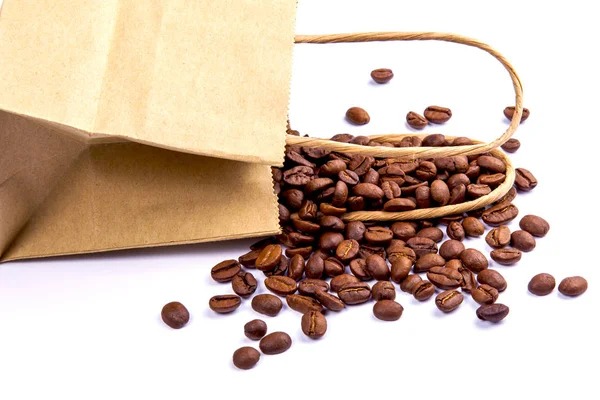 Seeds of coffee are scattered near a paper package on a white table