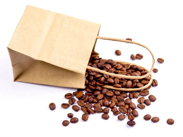 Seeds of coffee are scattered near a paper package on a white table