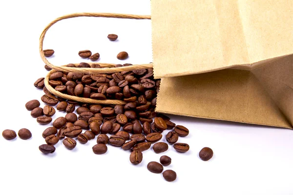 Seeds of coffee are scattered near a paper package on a white table