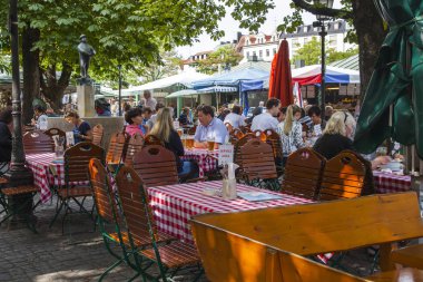 Münih, Almanya, on 16 Ağustos 2018. İnsanlar Bavyera'nın başkentinin eski şehrindeki sokak kafesinin masalarında yemek yiyip dinleniyor. 