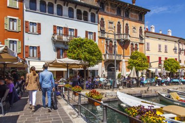 Desenzano del Garda, İtalya, 27 Nisan 2019. Güzel setten pitoresk koy. İnsanlar kafenin masalarında yemek yiyip dinleniyor. Tekneler setin yakınında demirledi..