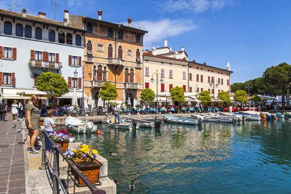 Desenzano del Garda, İtalya, 27 Nisan 2019. Güzel setten pitoresk koy. İnsanlar kafenin masalarında yemek yiyip dinleniyor. Tekneler setin yakınında demirledi..