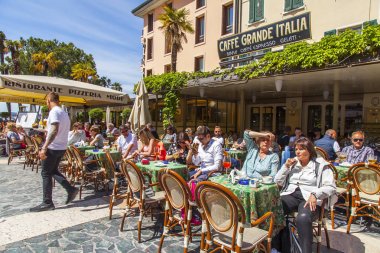 Sirmione, İtalya, 27 Nisan 2019 tarihinde. İnsanlar sokak kafenin masalarında yemek yiyip dinleniyor. 