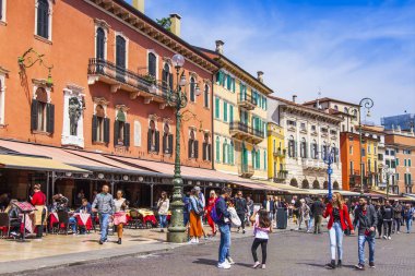 Verona, İtalya, 27 Nisan 2019 tarihinde. İnsanlar şehrin merkezi meydanlarından biri olan Piazza Bra Meydanı'ndaki sokak kafesinin masalarında yemek yiyip dinleniyor.