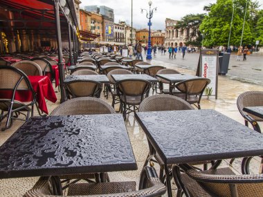 Verona, İtalya, 27 Nisan 2019 tarihinde. İnsanlar, akşam saatlerinde yağmurdan sonra şehrin merkezi meydanlarından biri olan Piazza Bra Meydanı'na doğru gidiyor. Bir yağmurdan ıslak pitoresk sokak kafe Tablolar.