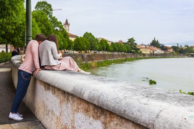 Verona, İtalya, 24 Nisan 2019 tarihinde. Adige Nehri'nin ve setlerinin panoramik manzarası. Gençler manzaraya hayran